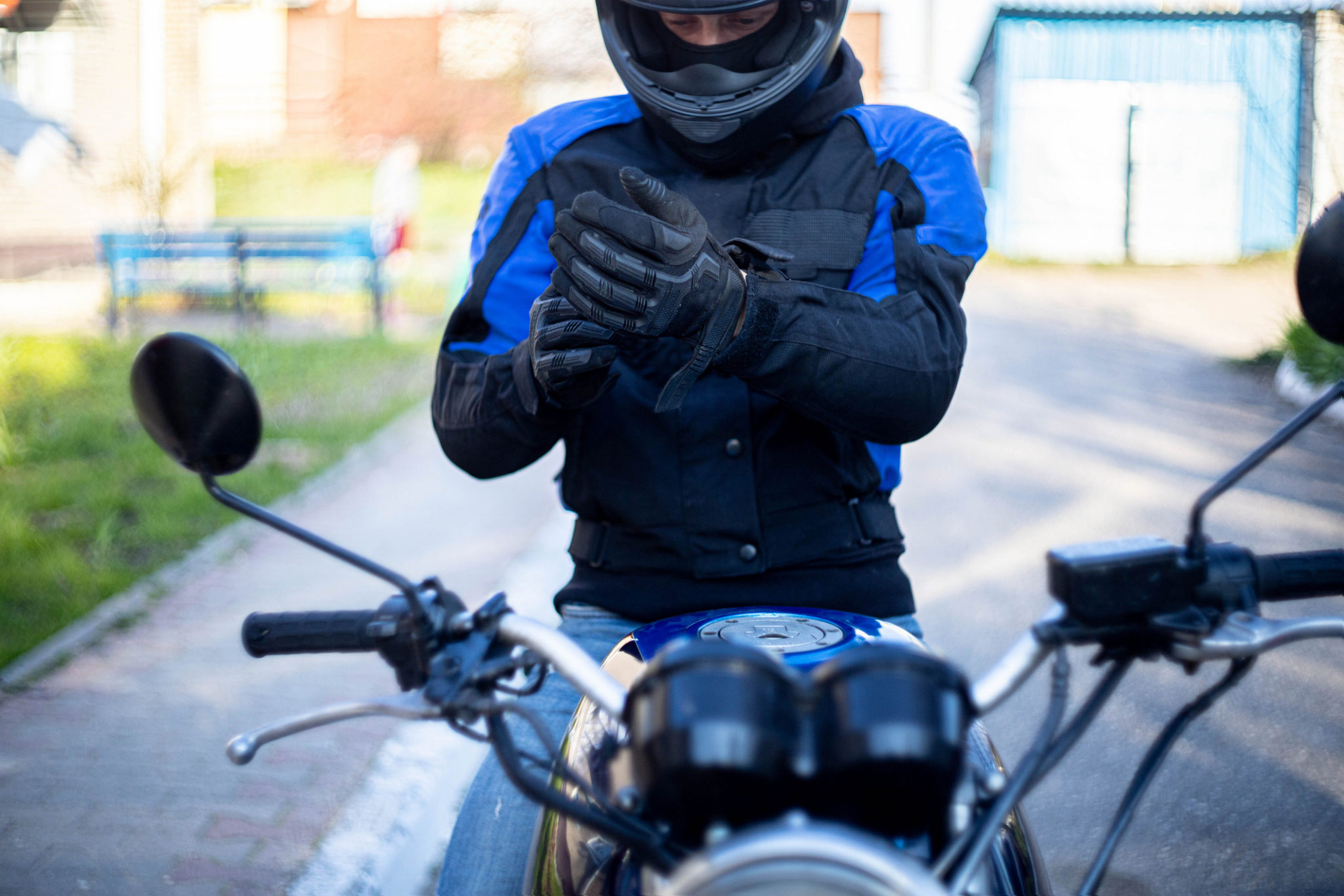 male motorcyclist in a helmet and gear puts on leather gloves.