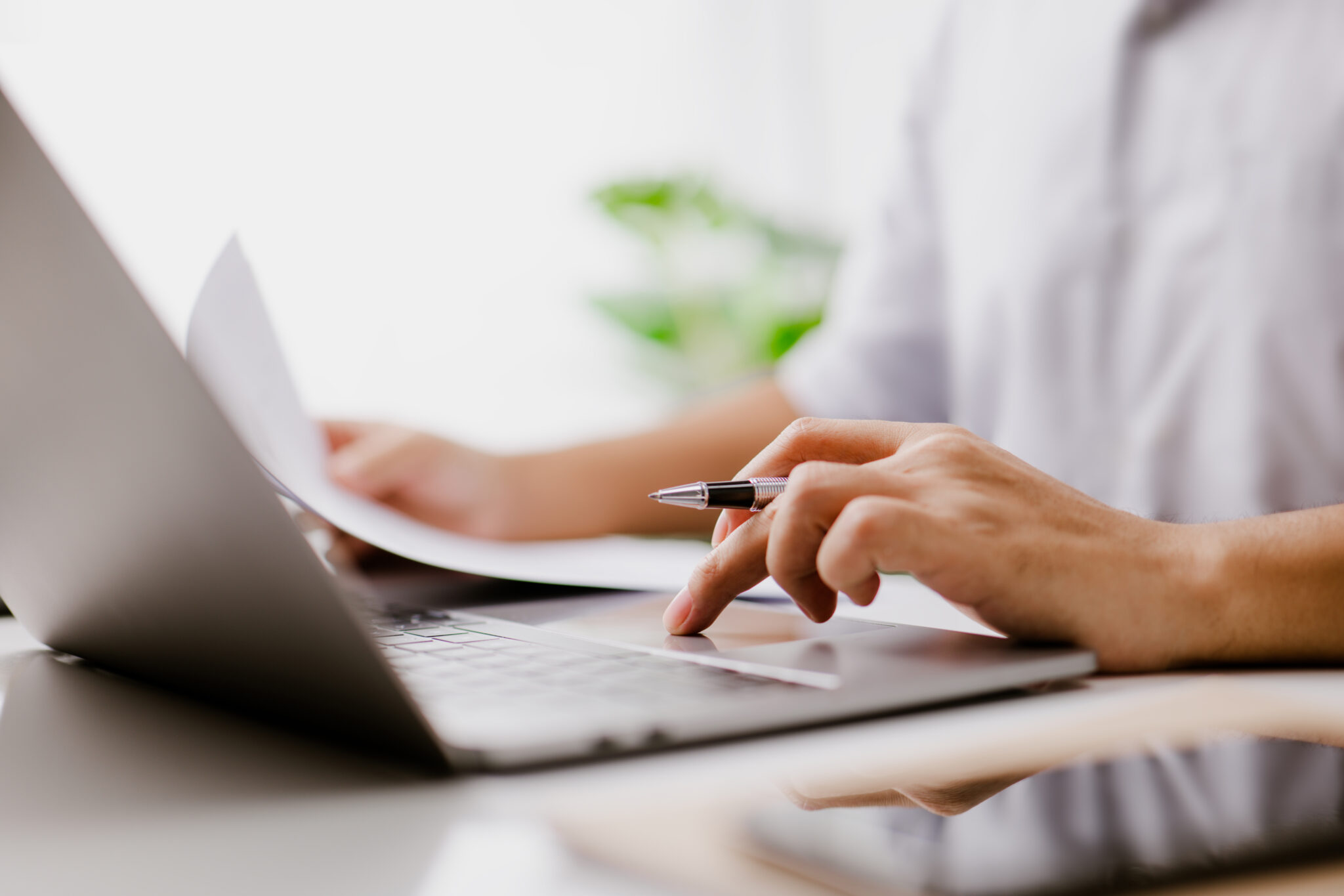 Businessman hand is on the trackpad, typing on a laptop keyboard, while reading a business document. In a modern office, a corporate man, a lawyer, works. Concept of business and technology.